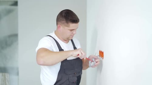 Male worker professional qualified electrician installs electrical outlet in apartment after repair.