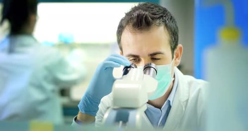 jeune médecin scientifique de sexe masculin propre regardant à travers le microscope pour agrandir les cellules de batteries virales