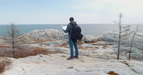 Man Reads Map on Rocky Ocean Coastline