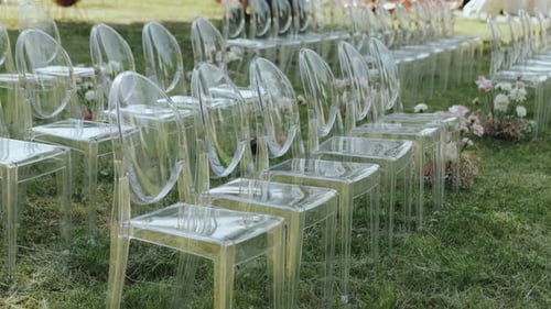 Many Transparent Plastic Chairs in Front of the Arch Chair on Green Lawn Outdoor Wedding Ceremony in
