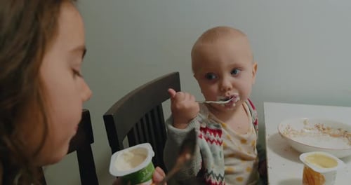 Little Child Eating With Sister at Table Indoors