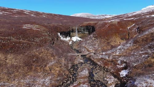 Skyline Mountain Background in Svartifoss Icelandic Waterfalls Aerial Drone Zoom into cascading wate