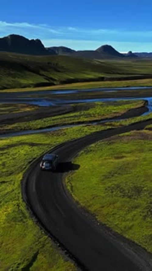 Vertical drone follow of a 4x4 SUV driving a curved gravel road beside braided river channels