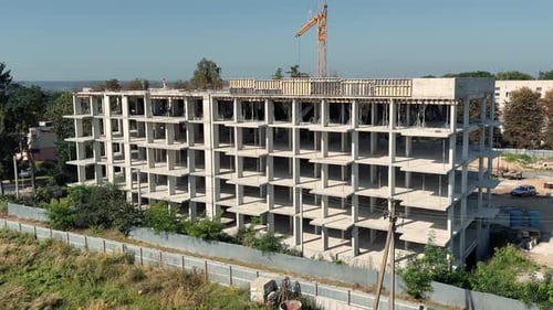 Vista de cerca de los trabajadores de la estructura de construcción de concreto sin terminar en el piso superior y la grúa de la torre detrás