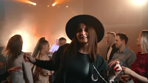 Stilvolle brünette Frau mit Hut tanzt auf einer Musikparty im Nachtclub, überfüllte beleuchtete Tanzfläche
