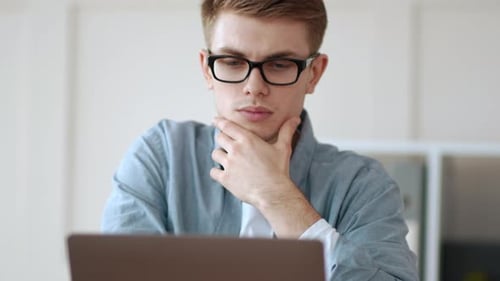 Nachdenklicher Typ, der Hand am Kinn hält und im Heimbüro arbeitet
