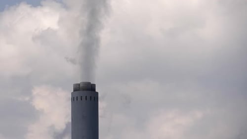 Single tall industrial smoke stack chimney pours smoke into cloudy sky