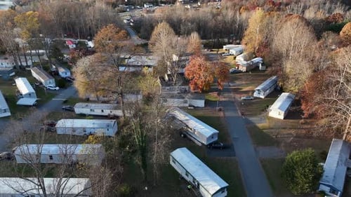 Aerial view showing American mobile home park nestled among fall trees, warm sun casting soft light