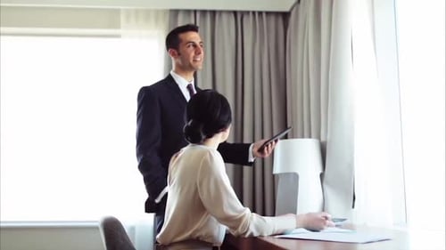 Hombre y mujer hispanos trabajan en equipo con papeles y tabletas en una habitación de hotel