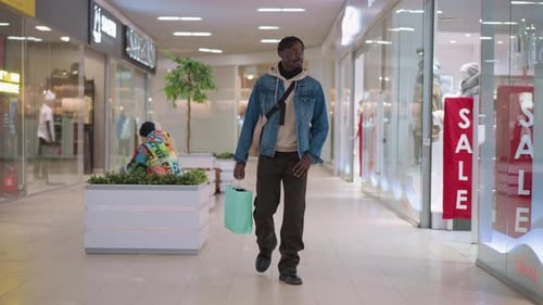 Male Shopper Walking Down Mall Corridor Carrying Green Shopping Bag