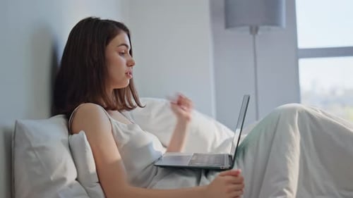 Glückliche Frau beim Videotelefonieren mit Laptop im Bett am heimischen Wochenendmorgen in Nahaufnahme