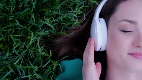 Ein Mädchen hört im Sommer auf einer Wiese Musik mit Kopfhörern, eine Nahaufnahme des Gesichts eines Mädchens
