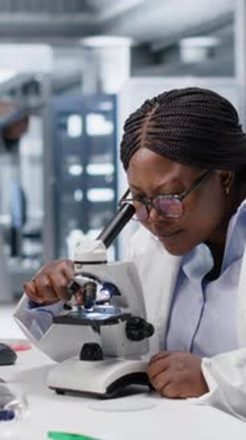 Vertical Video African American Scientist Focuses on a Microscope with Tray of Samples
