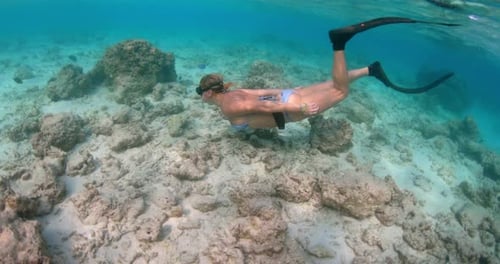 A woman in a bright bikini with swim fins enjoying snorkeling in the middle of corals and sea life