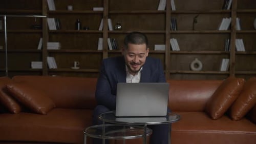 Asian Businessman on a Video Conference Call Using Laptop Computer in His Loft Office