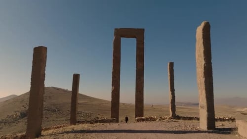 Drone filmé en arrière entre des colonnes carrées en pierre depuis une arche massive en pierre avec une femme touristique