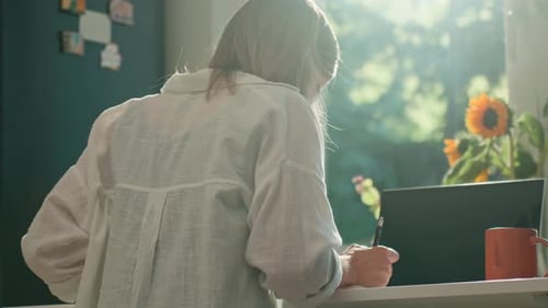 Woman Writing at Desk with Laptop and Sunlight