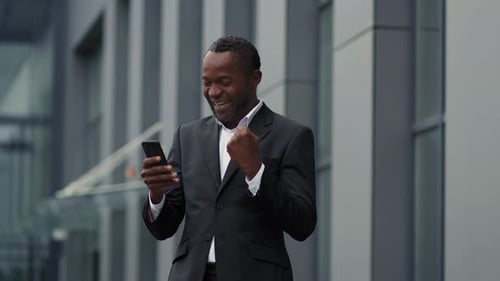 Excited Man Celebrates Success with Phone Outside Office
