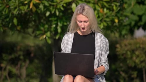 Beautiful young freelance woman with laptop lying sitting on bench in park.