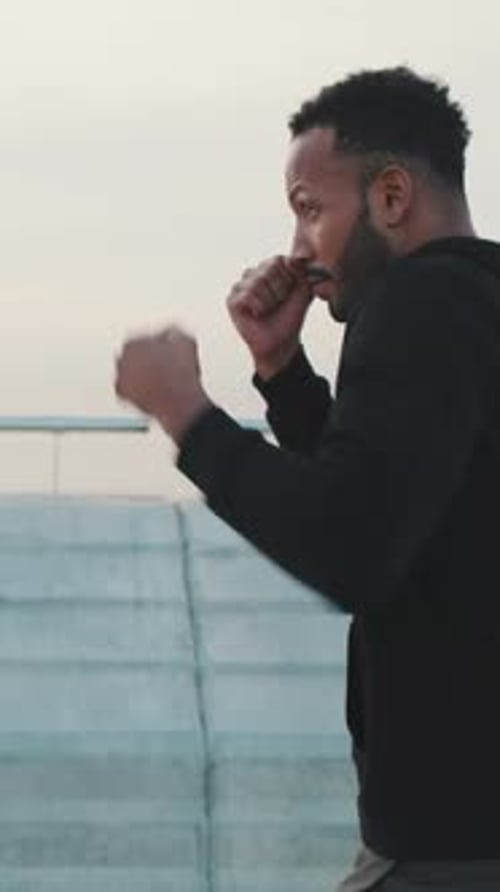 Young athlete boxer practicing punching technique while standing on the embankment