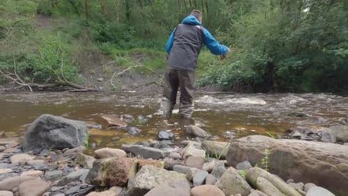 Static shot of a fisherman fly fishing trying to catch fish in fast flowing water