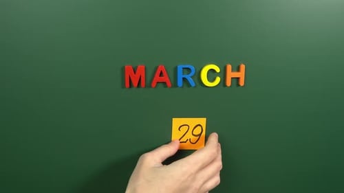 Hand sticking a sticker 29 March calendar day on school board. 29 date of March. Twenty ninth day