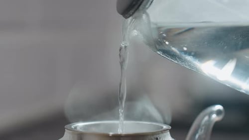 Close Up Pouring Hot Water Into Glass Kettle with Steam Rising