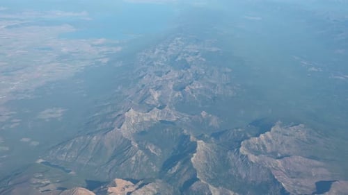 High altitude aerial view of rugged dry mountain landscape and valleys beneath a hazy blue sky
