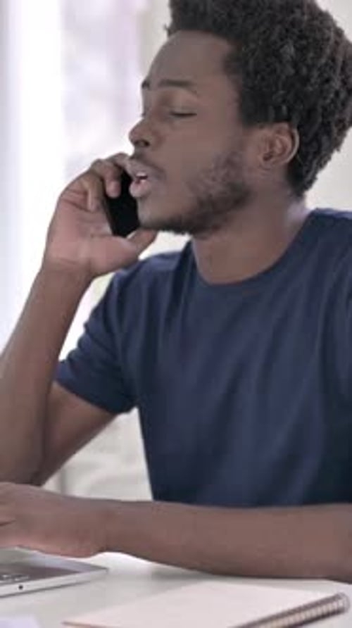 Young Man Talking on Phone While Using Laptop