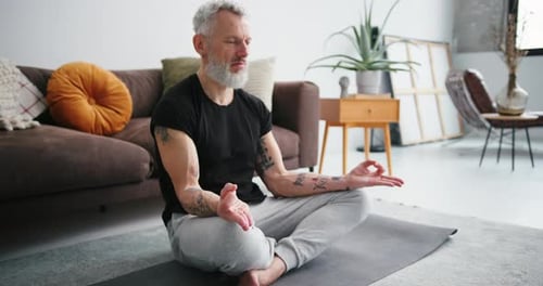 Bearded Man Meditating at Home on Yoga Mat