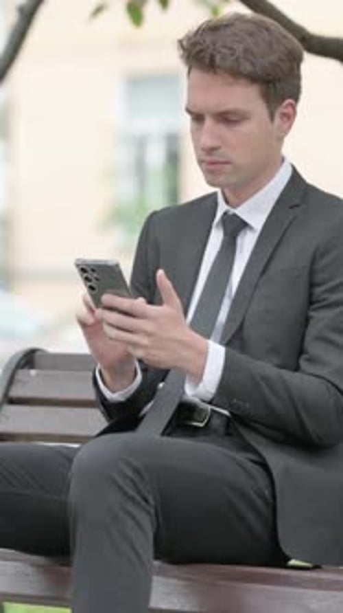 Young Man Using Smartphone While Sitting on Bench