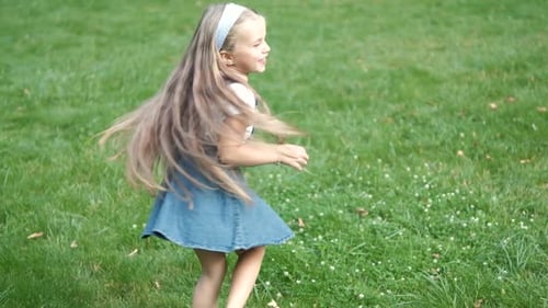 Little Child Girl Having Fun Turning Around on Green Grass in Summer Park