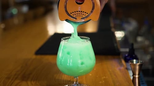 Pouring a Green Cocktail Through a Strainer