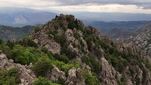 Drone footage of a rocky peak and a green forest in the Pyrenees mountains.