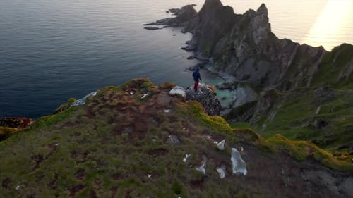 Stunning orbiting aerial view of a person walking on the edge of a cliff looking down on the rocky c