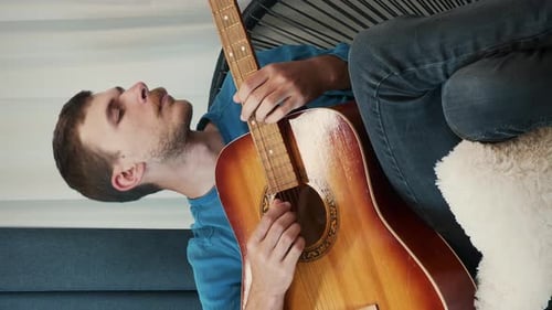 Young Adult Practices Acoustic Guitar at Home