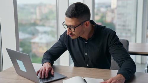 Office male employee working at laptop sitting at desk.