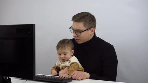 The IT Specialist Works Remotely with His Son in His Arms