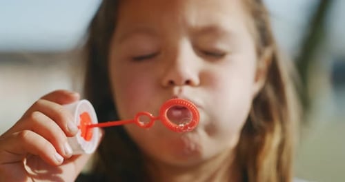 Authentic close up shot of little girl blowing soap bubbles in spring park on a sunny day.