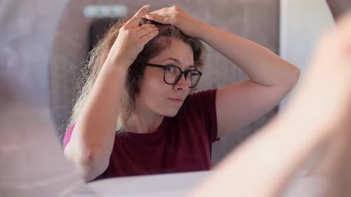 Woman Examining Gray Hair Roots in Mirror