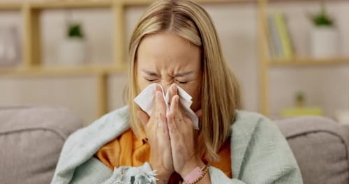 Woman Sits on Couch and Sneezes into Tissue