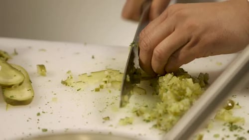 Nahaufnahme von Händen beim Hacken von Gurken auf einem weißen Schneidebrett, Küchenvorbereitungsszene
