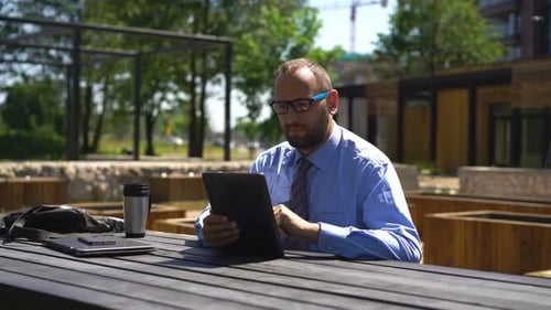 Businessman Working On Tablet Computer Sitting In City Park