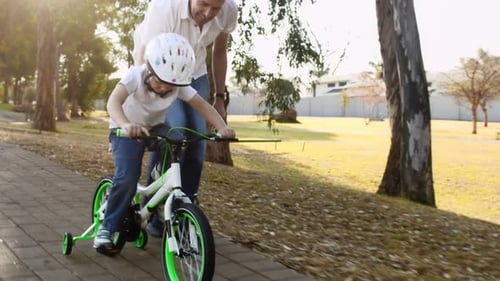 Father teaches son to ride bike on park pathway with safety helmet steadicam shot