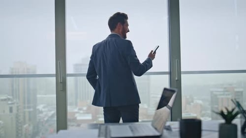 Business Manager Speaking Cellphone Looking at Panoramic Window Office Back View