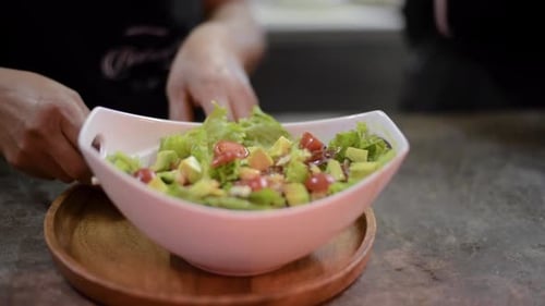 Woman chef cook preparing a salad adding slices of avocado at a local restaurant diner cafe in Mexic