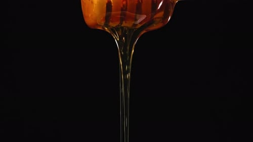Close Up Orange Honey Flows Down Wooden Spoon On Black Isolated Background