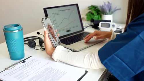 Woman Video Calling Senior Doctor While Typing on Laptop