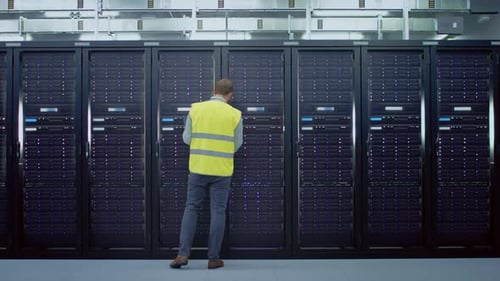 Bearded IT Administrator in High Visibility Vest is Opening the Door to the Server Rack with a Key.