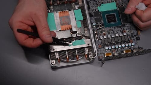 Top View of Repairman Male Using Tweezers to Carefully Remove Old Thermal Paste From Graphics Card